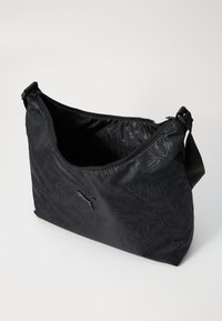 Schwarze Schultertasche aus Stoff mit einem Reißverschluss, die auf der Außenseite mit einem schlichten Puma-Logo und Branding in passendem dunklen Druck versehen ist.