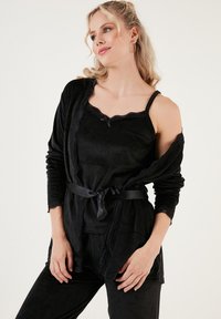 Crni komplet za opuštanje koji se sastoji od topa na bretele i ovijene haljine. Mekana tekstura, čipkasti detalji i satenski pojas na ovijenju. Elegantan i jednostavan dizajn.