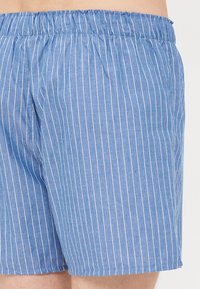 Pantaloni corti a righe blu con cintura elasticizzata, realizzati in tessuto leggero. Presentano righe bianche verticali e una vestibilità rilassata.
