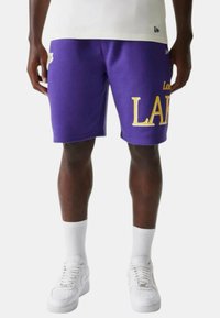 Pantaloni corti viola realizzati in tessuto morbido, con la scritta 'Los Lakers' in giallo. Taglio sopra il ginocchio, abbinati a calze bianche e sneakers.