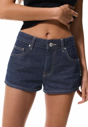 Shorts en denim foncé avec une taille ajustée, des coutures soignées, des poches avant et une fermeture à bouton en métal. Texture lisse et longueur courte.