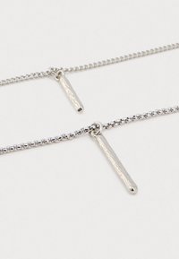 Δύο ασημένια κολιέ αλυσίδας με βαρελάκια με σφυρηλατημένα κάθετα μπαρ σε λευκό φόντο.