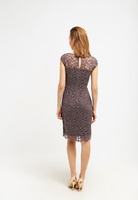 Robe en dentelle mauve foncé, longueur genou avec manches courtes et détail dos en forme de goutte. Présente des motifs floraux et une silhouette ajustée.