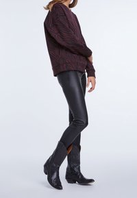 Felpa bordeaux con stampa zebra, abbinata a pantaloni fitti in ecopelle neri e stivali da cowboy neri con cuciture decorative.