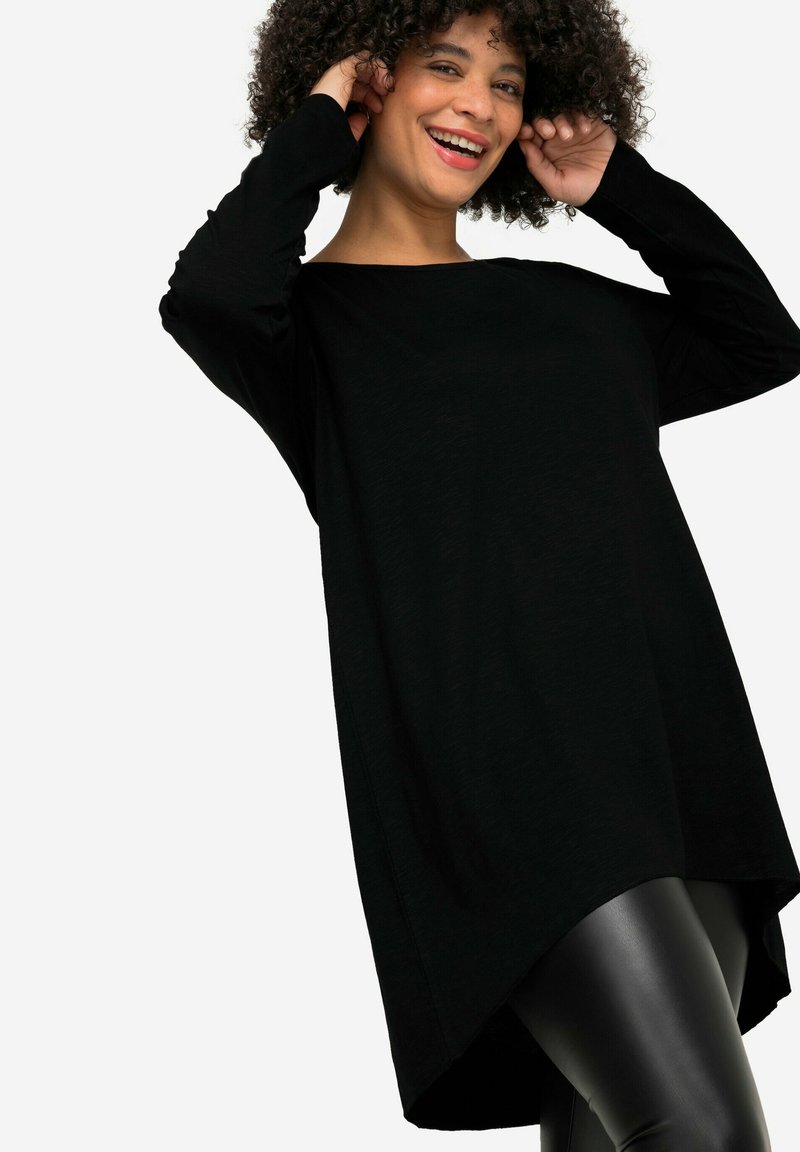 Black long-sleeve top with a wide neckline, relaxed fit, and asymmetrical hem, paired with shiny black leggings. Smooth texture.