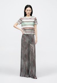 Top cu mâneci scurte și model zigzag multicolor, asortat cu pantaloni largi plisate, lucioși, în argintiu cu accente roșii. Textură netedă.