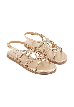 Sandalias con tiras y acabado en oro metálico. Presenta detalles trenzados y una correa de tobillo ajustable. Suela plana con textura antideslizante.