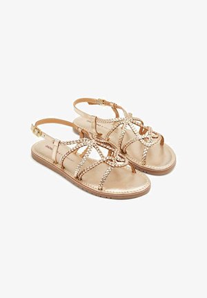 Sandalias con tiras y acabado en oro metálico. Presenta detalles trenzados y una correa de tobillo ajustable. Suela plana con textura antideslizante.