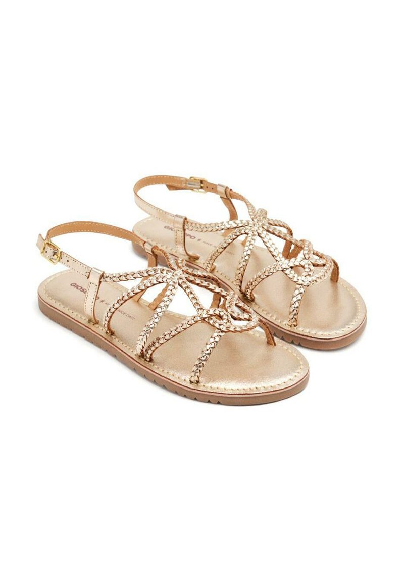 Sandalias con tiras y acabado en oro metálico. Presenta detalles trenzados y una correa de tobillo ajustable. Suela plana con textura antideslizante.