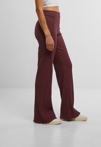 Des pantalons flared côtelés bordeaux avec une taille haute et un tissu texturé, associés à des baskets blanches pour un look décontracté.