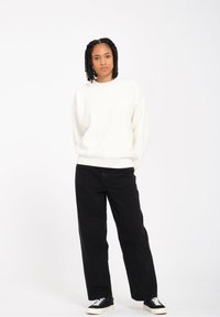 Hvid fleece sweatshirt med rund hals, afslappet pasform og ribbede mansjetter, parret med højtraljede sorte jeans og sorte sneakers.