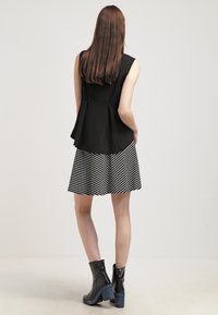 Svart ärmlös topp med en utsvängd design, i kombination med en svart och vit randig kjol. Svarta ankelstövlar med en blå klack.
