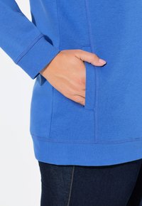 Blå sweatshirt med en mjuk textur, med en hand i fickan, ribbade ärmslut och rak fåll.