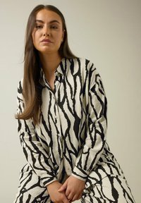 Camisa de botones con estampado de cebra en crema y negro, que presenta mangas largas y un corte holgado, con una tela texturizada y cuello clásico.