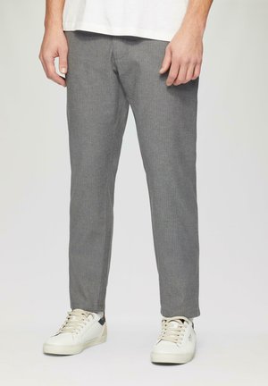 Pantalons gris avec un motif en chevrons subtil, coupe fuselée et texture douce. Associés à des baskets basses blanches et beiges.