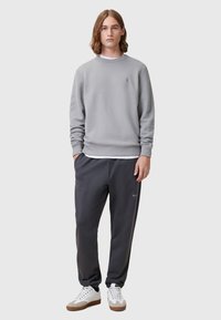 Grijze sweatshirt met ronde hals, geribbelde mouwen en bijpassende grijze joggers. Witte sneakers met beige accenten maken de outfit compleet.