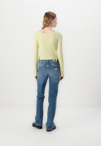 Ribbad ljusgrön tröja med öppen rygg, i kombination med mid-blå raka jeans med dekorationer på bakfickorna.