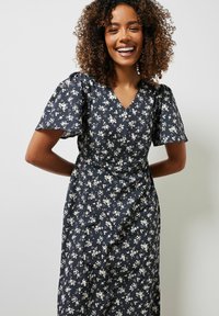 Vestido de corte envolvente en azul marino con mangas cortas abullonadas, que presenta un escote en V, un patrón floral blanco y una tela texturizada.