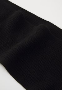 Tecido preto de malha com uma textura canelada, apresentado sobre um fundo branco, mostrando dobras suaves e padrões elevados.