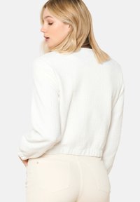 Kratka bela teksturirana jakna z dolžnimi rokavi in rebrastimi manšetami. Ima gladek izrez in oprijet rob.