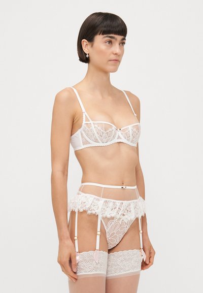 Ensemble de lingerie en dentelle blanche composé d'un bralette avec des bonnets semi-transparents, d'une ceinture porte-jarretelles assortie avec un bord en dentelle, et de bas montants en dentelle avec des motifs floraux.