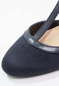 Gros plan sur une chaussure plate pour femme en daim bleu marine avec une bordure en cuir et une bride sur le dessus.