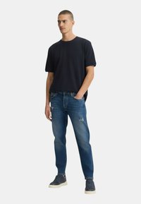 T-shirt navy a girocollo con maniche corte, abbinato a jeans di lavaggio medio con effetti di usura. Indossato con sneakers navy.