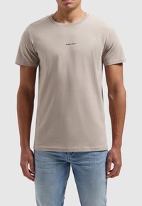 Lichtbeige katoenen t-shirt met korte mouwen en een ronde hals. Heeft een kleine zwarte tekstprint "PURE PATH" op de borst.