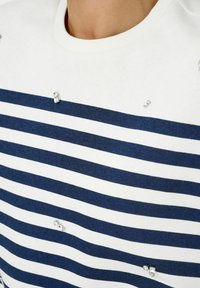 Randig tröja i vitt och marinblått med rund halsringning; har strassdetaljer på framsidan, mjuk stickad textur.