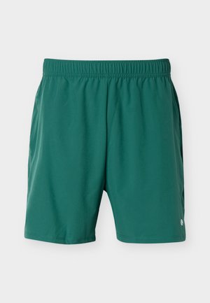 Grønne treningsshorts med elastisk midjebånd, sidelommer og en liten hvit logo nær kanten på høyre ben.