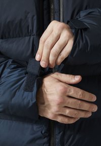 Chaqueta acolchada en color navy con cremallera frontal y puños ajustables de Velcro. La tela tiene una textura suave y ligeramente brillante.