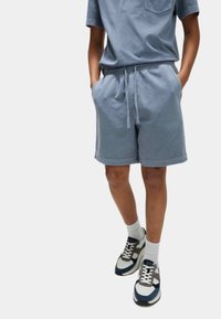 Hellblaue Baumwollshorts mit einem elastischen Bund und seitlichen Taschen, kombiniert mit weißen Socken und navy, grau und weißen Sneakers.