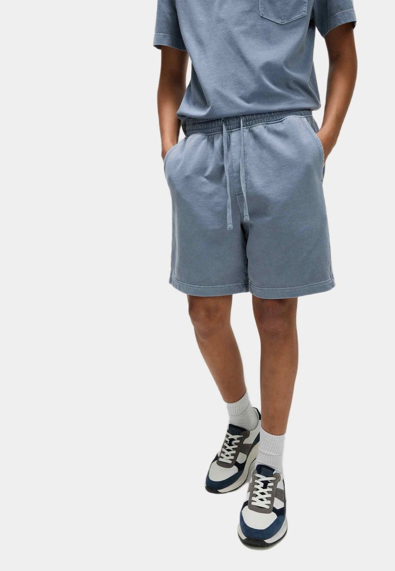 Hellblaue Baumwollshorts mit einem elastischen Bund und seitlichen Taschen, kombiniert mit weißen Socken und navy, grau und weißen Sneakers.
