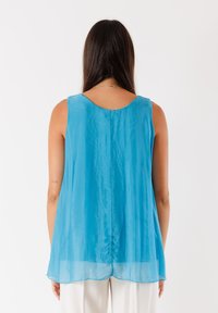 Top leggero senza maniche di un brillante blu, con scollatura a giro e un design fluido con un orlo posteriore leggermente più lungo.