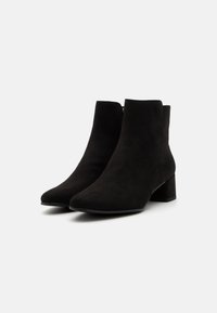 Botines negros de ante suave con puntera puntiaguda, tacón bajo y diseño minimalista. Presentan una textura lisa y sin herrajes visibles.