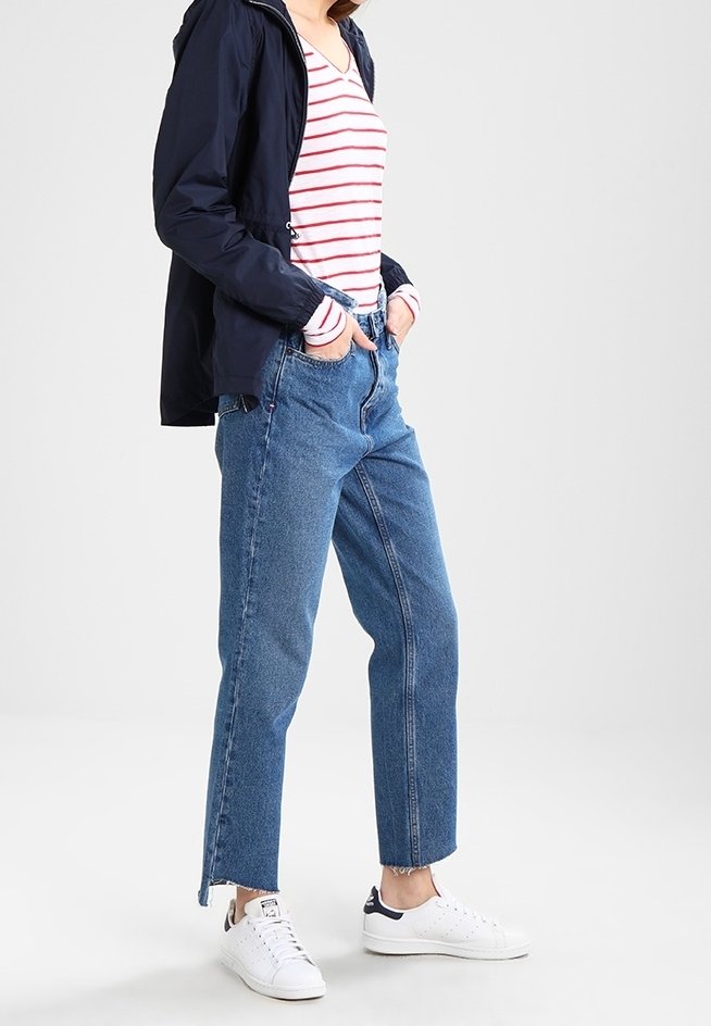 Marinblå lättviktsjacka, röd- och vitrandig långärmad tröja, blå högmidjade jeans och vita sneakers med marinblå detaljer.