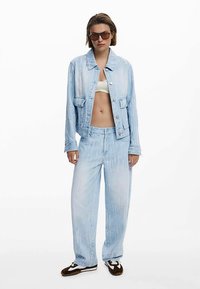 Vaaleansininen denimtakki ja sitä vastaavat housut, joissa on nappikiinnitys, kaksi etutaskua ja rento istuvuus. Valkoinen lyhyt toppi alla.