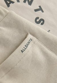 Beige Sweatshirt mit schwarzer Schrift. Verfügt über einen strukturierten Stoff und ein kleines Etikett mit "ALLSAINTS", das in dunklem Faden gestickt ist.