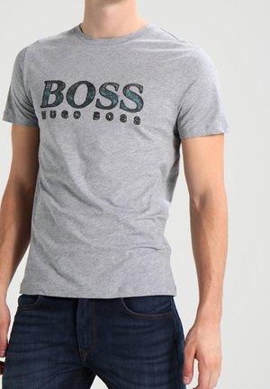 Mann trägt ein eng anliegendes graues T-Shirt mit "BOSS HUGO BOSS" auf der Brust bedruckt und dunkelblaue Jeans.