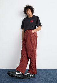 Sort kortærmet T-shirt med rød grafik, parret med løstsiddende bordeauxbukser og sorte sneakers med en hvid swoosh.