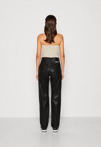Pantaloni in pelle neri a vita alta con un design a gamba dritta, dotati di due tasche posteriori e una leggera lucentezza. Indossati con una maglietta beige.