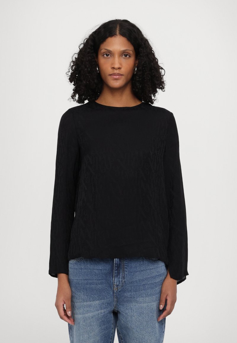 Svart langermet topp med en subtil mønstrete tekstur, rund hals og løs passform. Kombinert med lyseblå jeans.