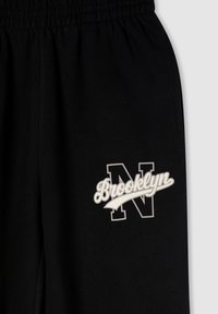 Czarne dresy z elastycznym pasem w talii, z białym logo z napisem "Brooklyn" oraz stylizowanym "N" na lewym udzie.