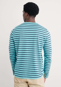 Cămașă cu mânecă lungă de culoare bleu deschis cu dungi orizontale bleumarin. Fabricată dintr-un material moale, are un guler rotund și un design lejer.