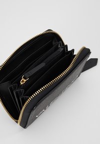 Portofel negru cu fermoar și accesorii aurii; dispune de mai multe sloturi pentru carduri, un buzunar pentru monede cu fermoar și un exterior texturat.