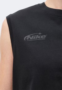 Κοντινό πλάνο ενός ατόμου που φοράει μαύρο αμάνικο μπλουζάκι Nike με το λογότυπο "Nike Running Engineering" σε σκούρο γκρι στο στήθος.