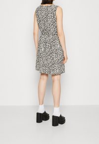 Mustaläiskukkakuosisessa mekossa on vyötäröä korostava ja levenevä helma. Mekossa on pyöreä pääntie ja hihattomat mallit. Asusteena korkeat kengät.