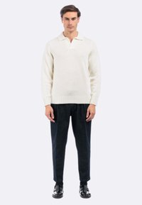 Maglione polo a maglia color crema con orlo e colletto a coste, abbinato a pantaloni scuri con texture e scarpe nere.