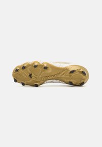Crampon de football avec une semelle extérieure texturée en or, des crampons noirs et un dessus blanc comportant un motif craquelé et une zone de protection renforcée.
