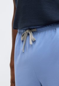 Calças de jogging azul claro com textura suave, apresentando um cós elástico e um cordão cinzento. Usadas com um top canelado azul-marinho.